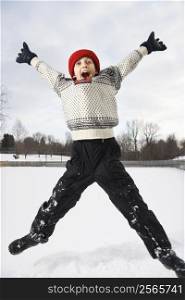 Excited Caucasian boy wearing sweater and red winter cap jumping in air with arms and legs outstretched.