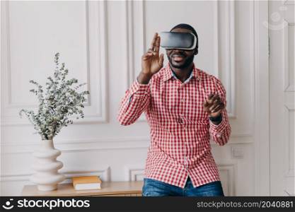 Excited cheerful african man wearing VR glasses totaly immersed in augmented reality of 3d games, black guy decided to take break from remote work online plunging into world of innovative technologies. Excited cheerful african man wearing VR glasses totaly immersed in augmented reality of 3d games