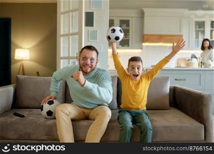 Excited father and little son cheering and watching football match on couch in living room at home. Happy family spending amazing time together. Excited father and son cheering and watching football match at home