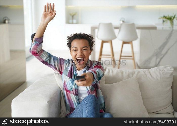 Excited football team fan is relaxing at home watching the game. African american teenage girl enjoying tv watching and shifts channels. Reality show or soccer match watching. Smart tv using.. Excited football team fan is relaxing at home watching the game. Soccer match watching.