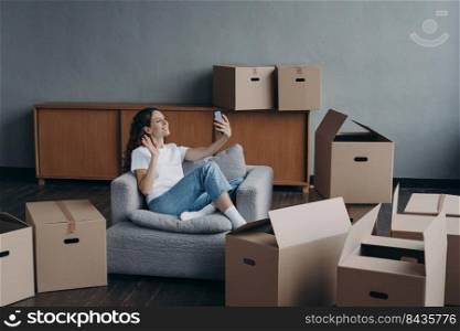 Excited girl having video call on phone in new apartment. Successful independent young woman. Mover shows her dream house. Mortgage loan and happy home owner concept.. Excited girl having video call in new apartment. Young woman shows her dream house.