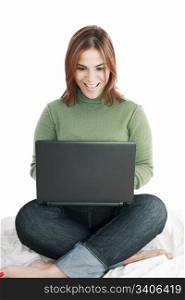 Excited girl in jeans with laptop sitting on her bed isolated