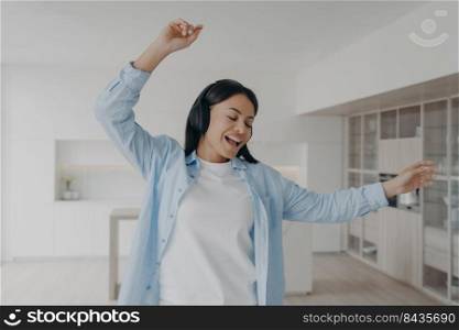 Excited girl is headphones is listening music, singing and dancing at home. European girl in wireless earphones enjoying music. Carefree weekend morning leisure. Positive emotions and freedom concept.. Excited girl in wireless earphones is headphones is listening music, singing and dancing at home.