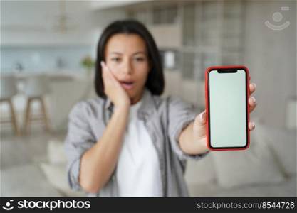 Excited girl shows phone display and touchscreen. Telephone advertising banner mockup. Handsome brunette european girl in living room. Communication technology and enjoyment, emotion expression.. Excited girl shows phone display and touchscreen. Communication technology advertising banner.
