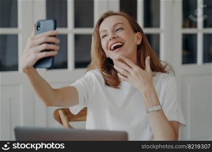 Excited happy mid adult businesswoman has video chat on phone from home. Attractive european lady is freelancer, entrepreneur or accountant and working in evening. Remote work concept.. Excited happy mid adult businesswoman has video chat on phone working in evening from home.