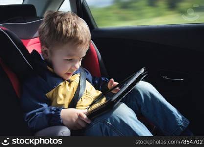 Excited little boy in the car playing with touchpad sitting in child safety seat