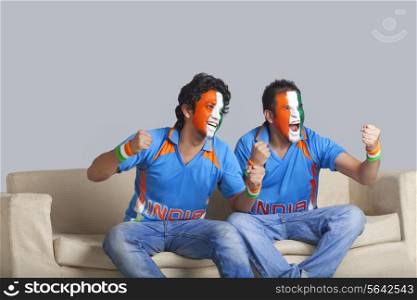 Excited male friends with face painted in Indian tricolor cheering with clenched fists