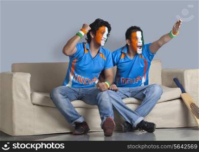 Excited male friends with face painted in Indian tricolor sitting together on sofa