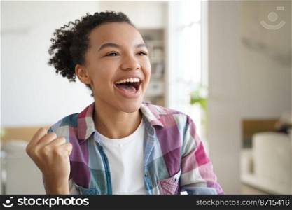 Excited mixed race teen girl makes yes winner hand gesture, celebrates success, personal achievement at home. Overjoyed young lady feeling happy received good news, screaming with raised clenched fist. Excited mixed race teen girl makes yes winner hand gesture, celebrates success, personal achievement