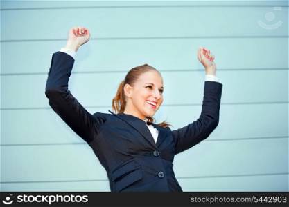Excited modern business woman standing at office building and rejoicing her success &#xA;