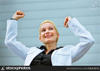 Excited modern business woman standing at office building and rejoicing her success &#xA;