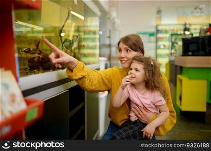 Excited mother and daughter looking on swimming fish in aquarium at pet shop. Happy family choosing new domestic animal at zoo store. Excited mother and daughter looking on swimming fish in aquarium at pet shop