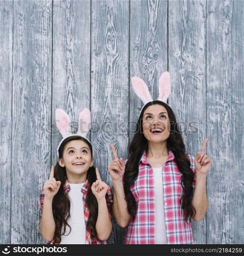 excited mother daughter with bunny ears pointing finger upward against wooden backdrop