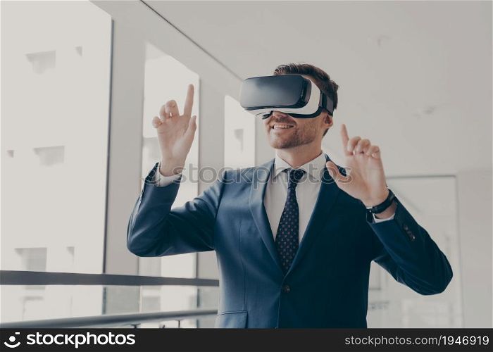 Excited office worker in vr headset or virtual reality goggles gesturing with hands, using innovative technologies for business at work, dressed in suit, smiling and touching objects in digital world. Excited office worker in vr headset or virtual reality goggles gesturing with hands