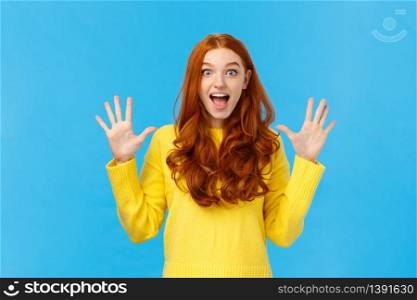 Excited, overwhelmed happy redhead cute girl in yellow sweater, screaming from joy telling about christmas gifts, showing ten fingers, order dozen products, standing joyful blue background.. Excited, overwhelmed happy redhead cute girl in yellow sweater, screaming from joy telling about christmas gifts, showing ten fingers, order dozen products, standing joyful blue background
