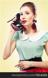 Excited pin-up girl using a shoe like a telephone holding it near her face and talking, yellow background.