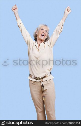 Excited senior woman in casuals cheering with arms raised against blue background