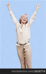 Excited senior woman in casuals cheering with arms raised against blue background
