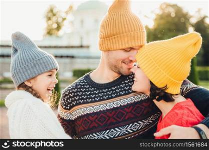 Excited small kid looks at her parents who are in love, going to kiss each other, have goos relationships, embrace. Affectionate woman and man support. Smiling little girl looks at father and mother