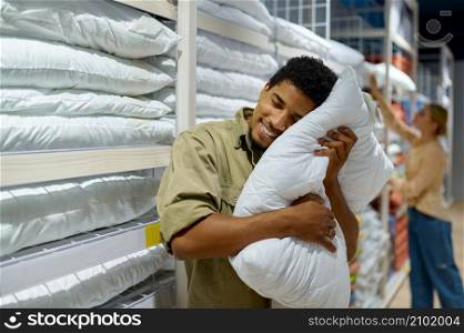 Excited smiling man purchaser holding soft pillow. Happy family couple shopping in textile market. Man purchaser holding pillow in textile shop