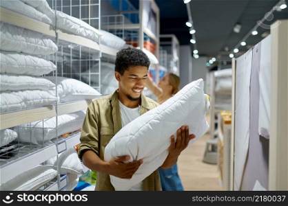 Excited smiling man purchaser holding soft pillow. Happy family couple shopping in textile market. Man purchaser holding pillow in textile shop