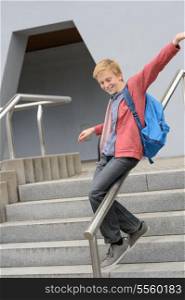 Excited teenage student sliding down handrail on school stairway