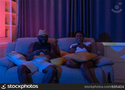 excited with emotional young couple, man and woman with joysticks playing video games in the dark night neon color light environment background at home