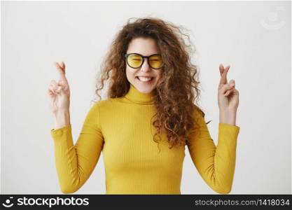 Excited woman in yellow sweater keeping fingers crossed, mouth wide open, waiting for special moment isolated on grey background. Excited woman in yellow sweater keeping fingers crossed, mouth wide open, waiting for special moment isolated on grey background.