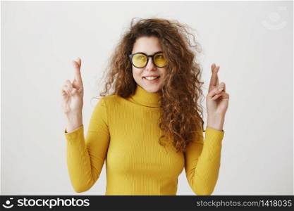 Excited woman in yellow sweater keeping fingers crossed, mouth wide open, waiting for special moment isolated on grey background. Excited woman in yellow sweater keeping fingers crossed, mouth wide open, waiting for special moment isolated on grey background.