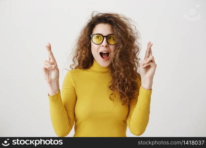 Excited woman in yellow sweater keeping fingers crossed, mouth wide open, waiting for special moment isolated on grey background. Excited woman in yellow sweater keeping fingers crossed, mouth wide open, waiting for special moment isolated on grey background.