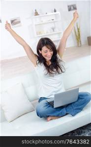excited woman sitting on sofa with laptop in her apartment