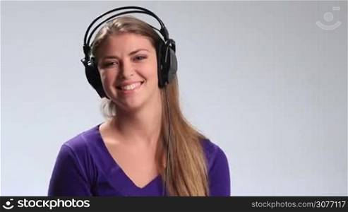 Excited young brunette woman in big black headphones having fun while listening to the music on white. Happy teenage girl making funny facial expressions, gesturing, flirting with camera while enjoying the sound of music on the mp3 player.