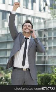 Excited young businessman using cell phone outside office
