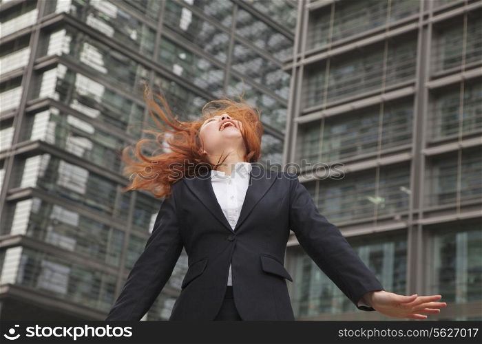 Excited young businesswoman looking up with wind blowing in her hair