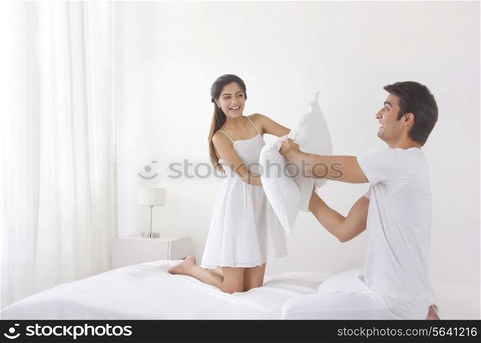 Excited young couple having pillow fight on bed