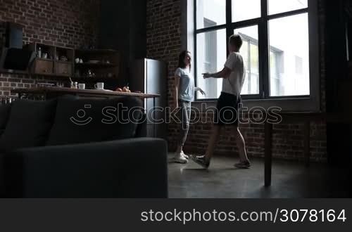 Excited young couple in love enjoying beautiful morning together in the kitchen, having fun and dancing. Two lovers spending leisure at home. Slow motion. Steadicam stabilized shot.