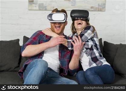 excited young couple sitting sofa using vr headset experiencing virtual reality