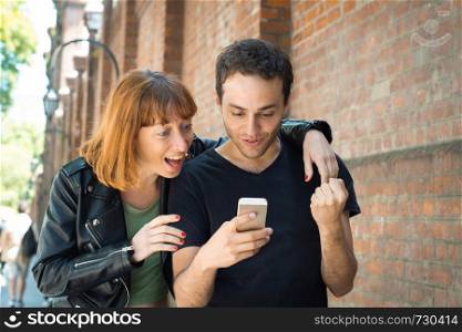 Excited young couple watching a smartphone outdoors. Good news
