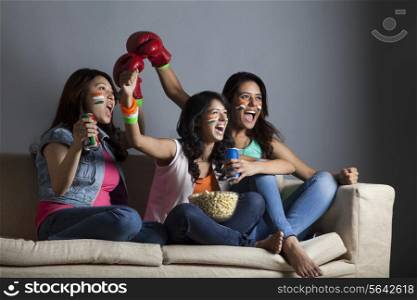 Excited young female friends watching boxing match together at home