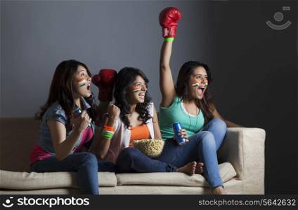 Excited young female friends watching boxing match together at home