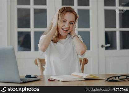 Excited young female surprised at unexpected good news, astonished woman sitting at laptop amazed by unbelievable email online store offer, holding head in amazement, sits in workplace.. Excited female holding head in amazement, rejoices at good news sits at laptop. Online store offer