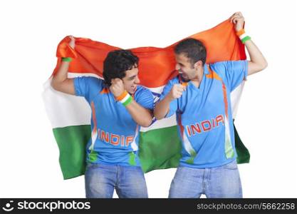 Excited young male friends in jerseys cheering while holding Indian flag over white background