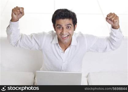 Excited young man gesturing success while using laptop