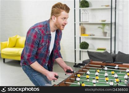 excited young man playing football table soccer game living room
