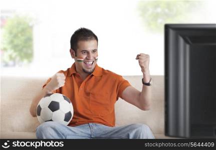 Excited young man with painted face cheering while watching soccer game on television