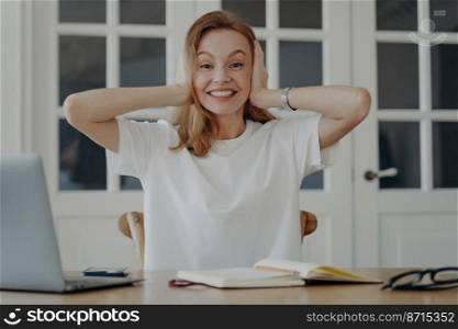 Excited young woman holding head in amazement, surprise, got good news, sitting at home office desk with laptop. Happy surprised smiling female student or employee rejoices in achievement in workplace. Excited young woman holding head in amazement, surprise, got good news, sitting at desk with laptop