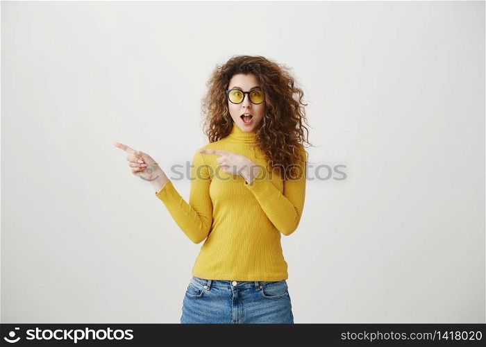 Excited young woman pointing her finger towards blank space isolated over grey background. Excited young woman pointing her finger towards blank space isolated over grey background.