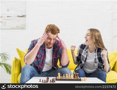 excited young woman sitting with her boyfriend cheering after winning chess game