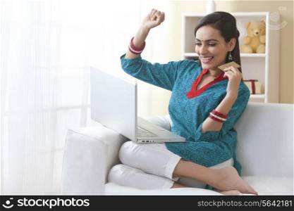 Excited young woman with credit card shopping online in living room