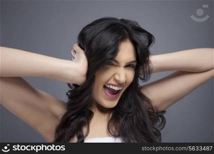 Excited young woman with her hands covering her ears over colored background